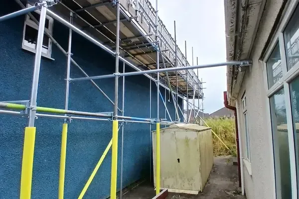 Yellow-sleeved scaffold standards against a freshly painted blue wall, ledgers running the length of the elevation.