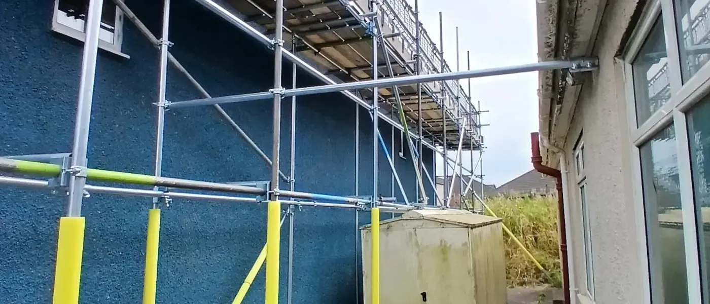 Yellow-sleeved scaffold standards against a freshly painted blue wall, ledgers running the length of the elevation.