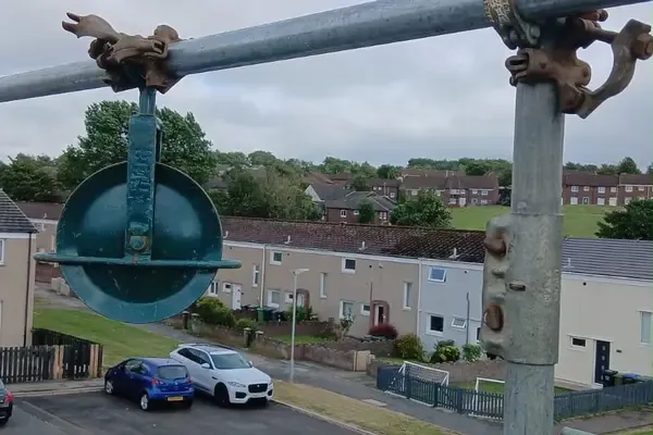 Close-up of a swivel coupler and pressed-steel fitting on a scaffold standard, a terraced street out of focus below.