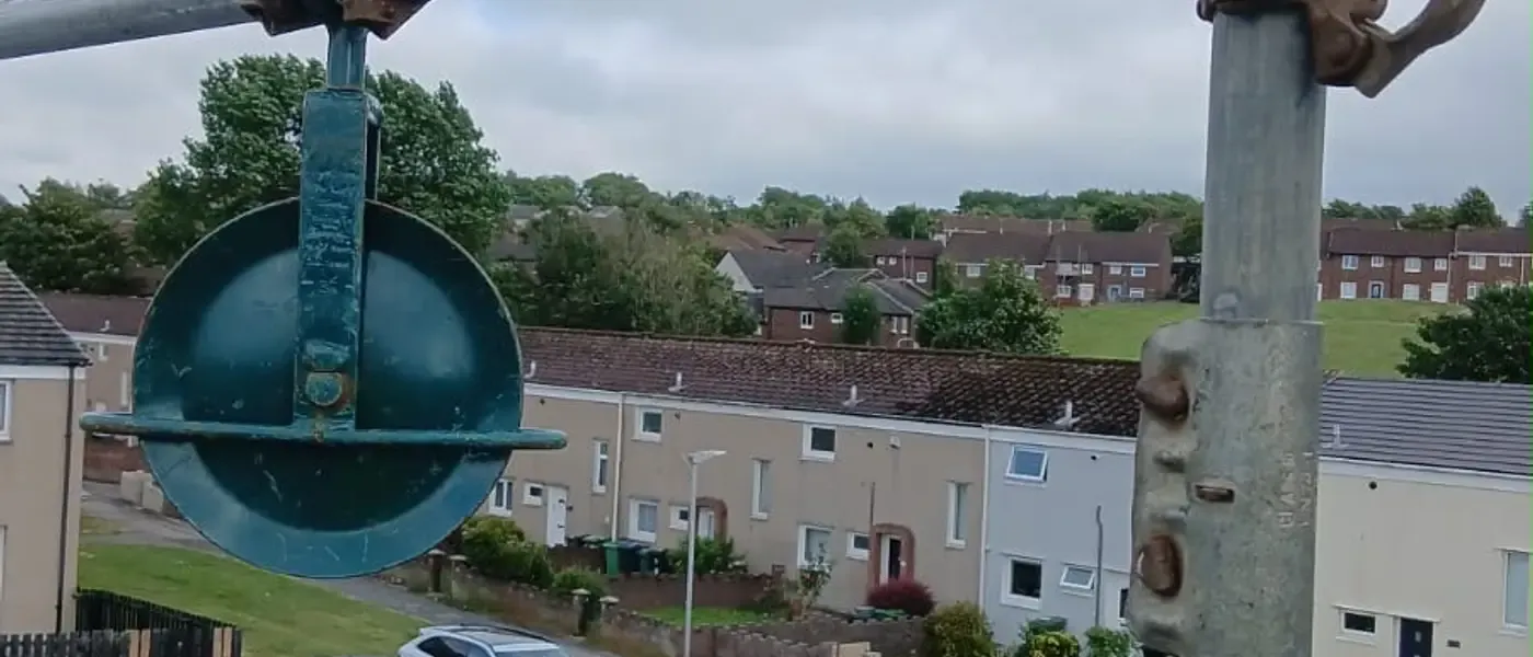 Close-up of a swivel coupler and pressed-steel fitting on a scaffold standard, a terraced street out of focus below.