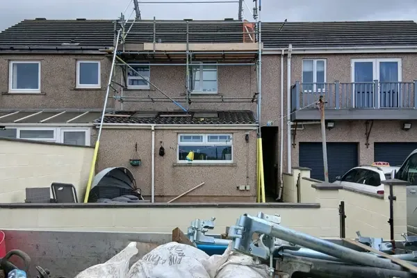Scaffold to the rear of a rendered terrace, with a loaded wagon and bagged materials in the foreground.