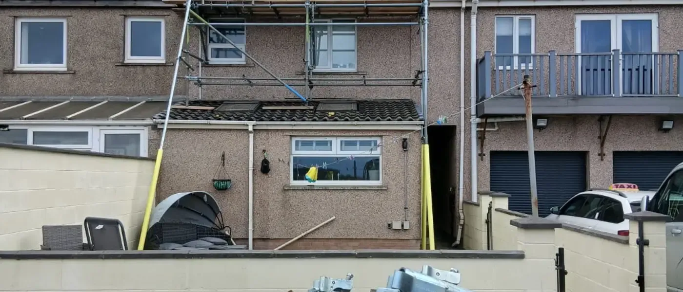 Scaffold to the rear of a rendered terrace, with a loaded wagon and bagged materials in the foreground.