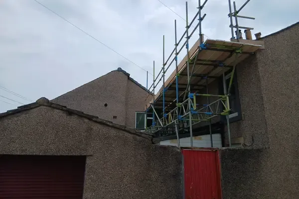 Boarded lift carried out over a garage roof to reach the eaves of the house behind.