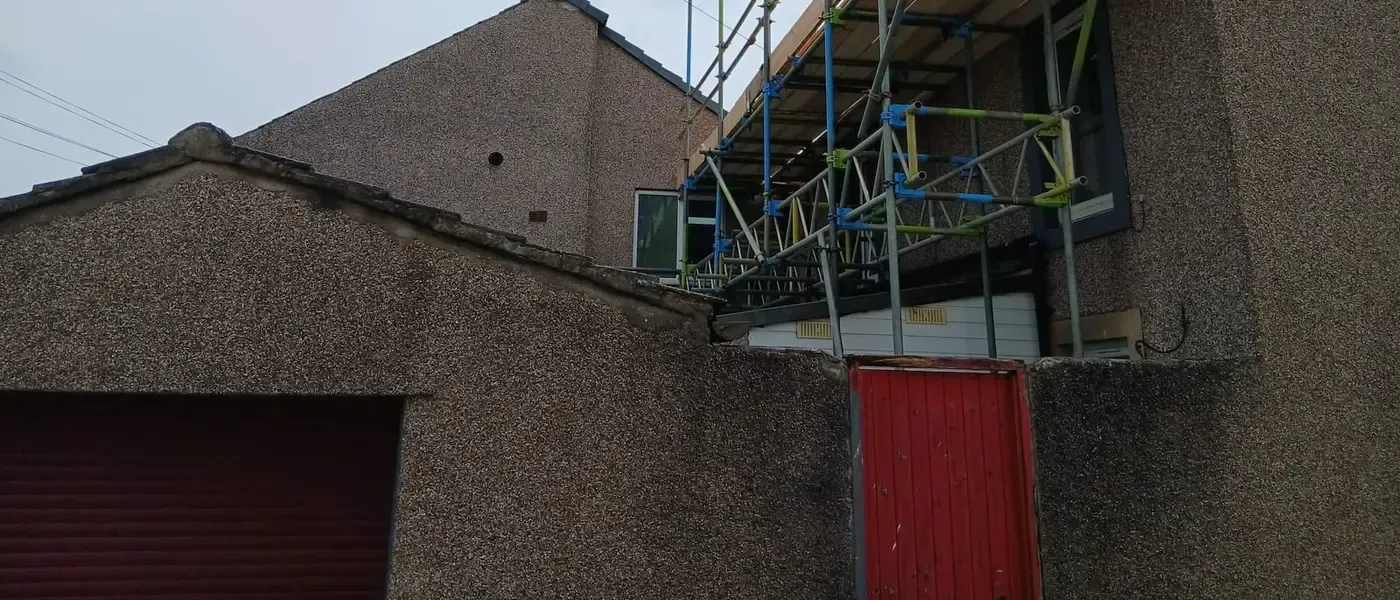 Boarded lift carried out over a garage roof to reach the eaves of the house behind.