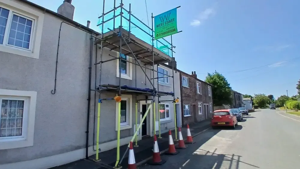Scaffold to a terrace on a working street, traffic cones lining the kerb and the footway kept open beneath.