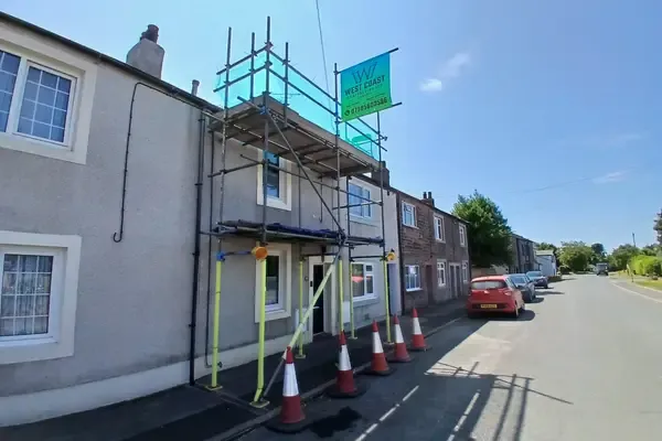 Scaffold to a terrace on a working street, traffic cones lining the kerb and the footway kept open beneath.