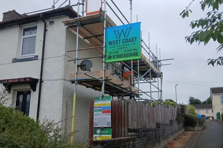 Banner on the top lift of a scaffold to a rendered house, with the inspection tag hanging at ground level.