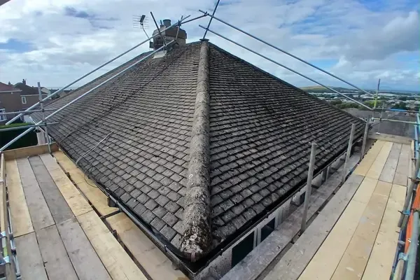 Hipped roof surrounded by a boarded scaffold platform, guardrails up and the coast on the horizon.