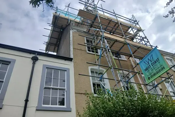 Scaffold to a rendered period house with sash windows, banner tied on and a boarded platform at eaves height.