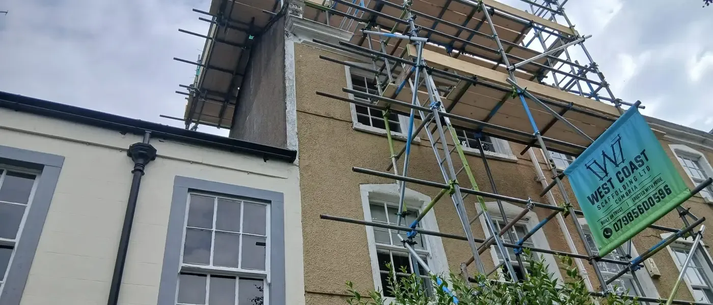 Scaffold to a rendered period house with sash windows, banner tied on and a boarded platform at eaves height.