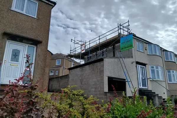 Scaffold to the rear elevation of a house, banner on the lift, garden and neighbouring roofs behind.