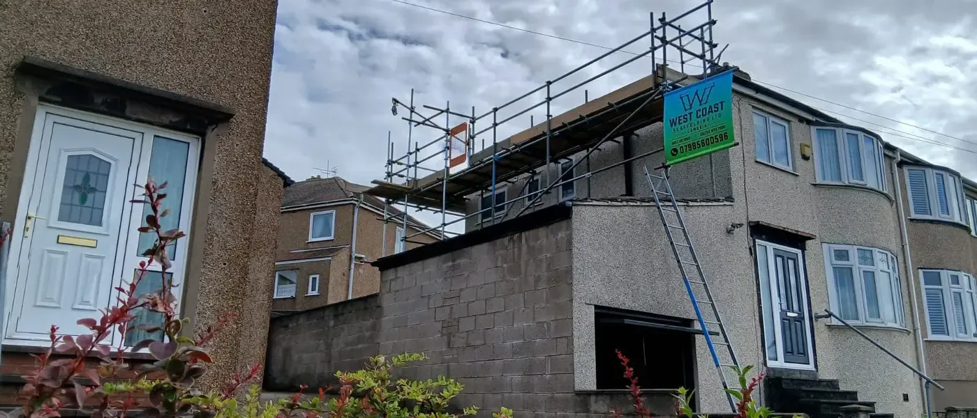 Scaffold to the rear elevation of a house, banner on the lift, garden and neighbouring roofs behind.