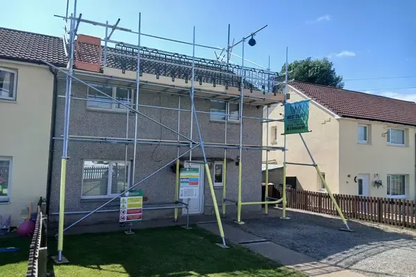 Scaffold to the front of a rendered semi, banner up, boarded lift at eaves level and the drive kept clear.