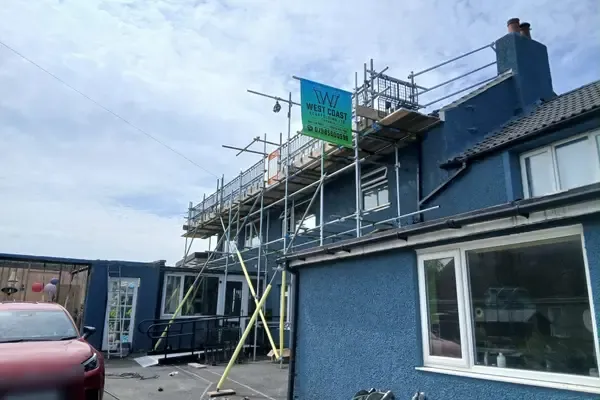 Scaffold to a blue-rendered house running up to the chimney, banner on the top lift.