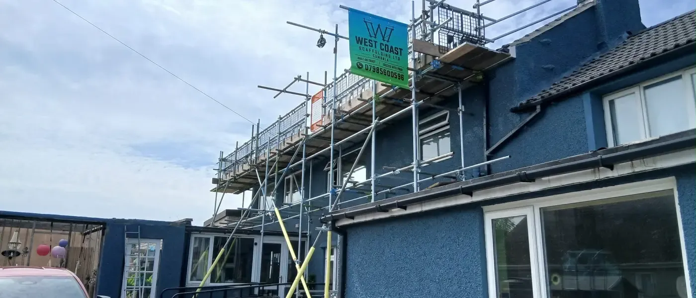 Scaffold to a blue-rendered house running up to the chimney, banner on the top lift.