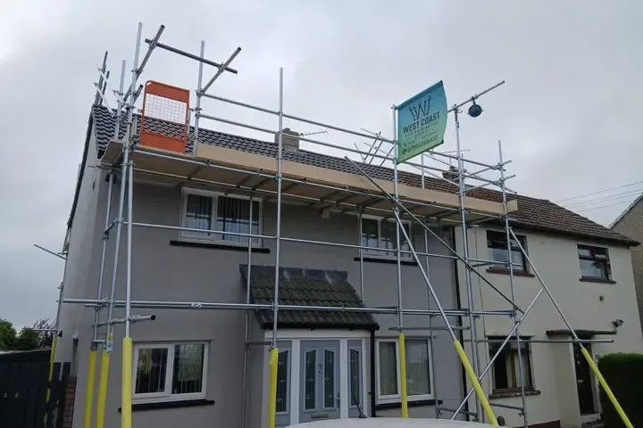 Scaffold across the front of a pair of semis, banner on the top lift and a boarded platform at eaves level.