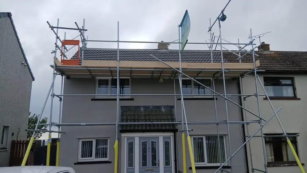 Scaffold to a rendered semi carried above the roof line, banner on the top lift and the platform boarded all round.