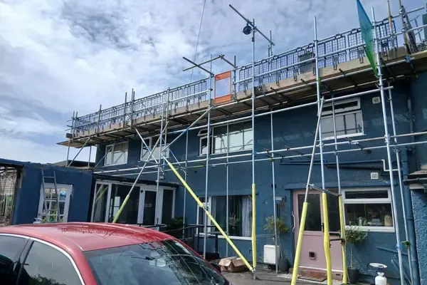 Scaffold running across blue-rendered terraces, boarded lift at eaves level with guardrails.