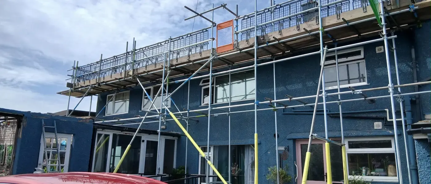 Scaffold running across blue-rendered terraces, boarded lift at eaves level with guardrails.
