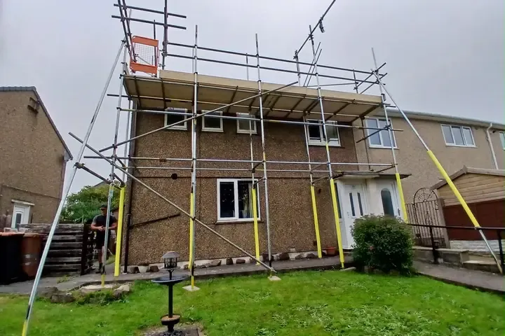 Scaffold to the rear of a semi seen from the garden, boarded lift and yellow-sleeved standards.