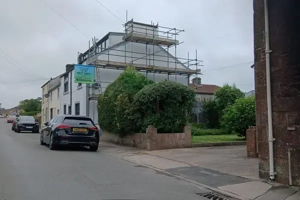 A scaffolded house on a West Cumbrian street, boarded lifts to the roof and parked cars along the kerb.